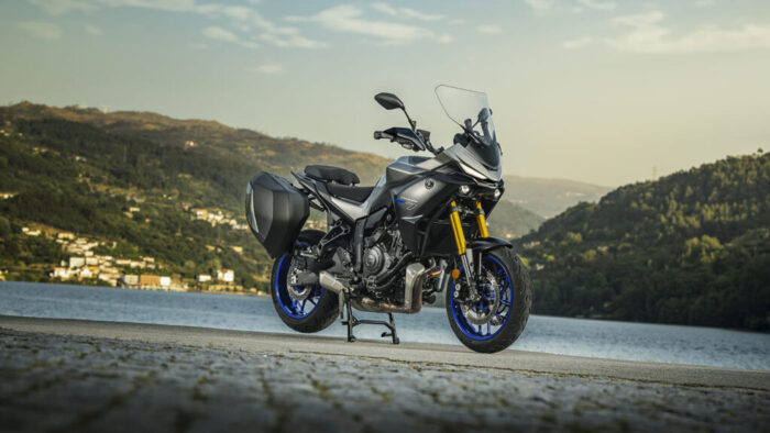 Yamaha Tracer 7 GT Y-AMT 2026 na sredinskem stojalu ob jezeru, potovalni motocikel s trdimi stranskimi kovčki in nastavljivim vetrobranom.