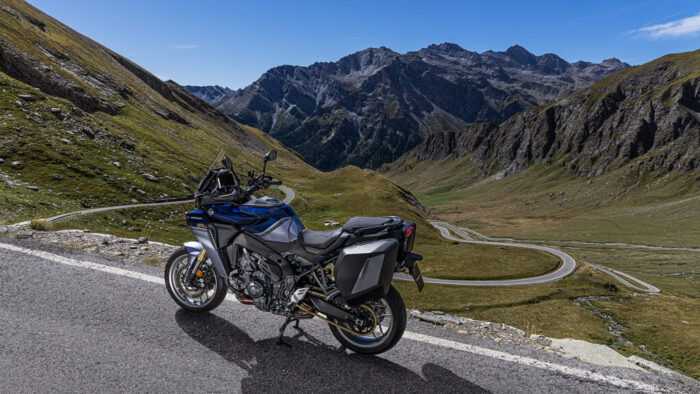 Yamaha Tracer 9 GT+ Y-AMT 2025 ob panoramski gorski cesti z zavitimi serpentinami v ozadju