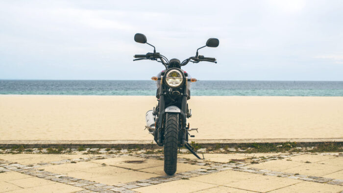 Yamaha XSR125 Legacy sprednji pogled ob obali, klasičen okrogel LED žaromet in zlate napere v retro slogu