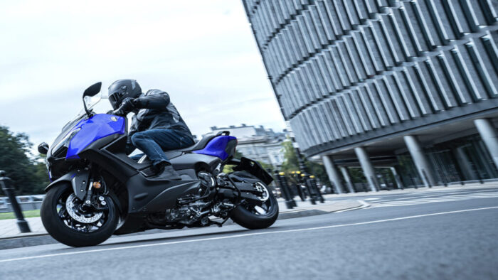 Yamaha TMAX 2026 v športnem nagibu med mestnimi ulicami, stabilen maxiskuter z natančno vodljivostjo.