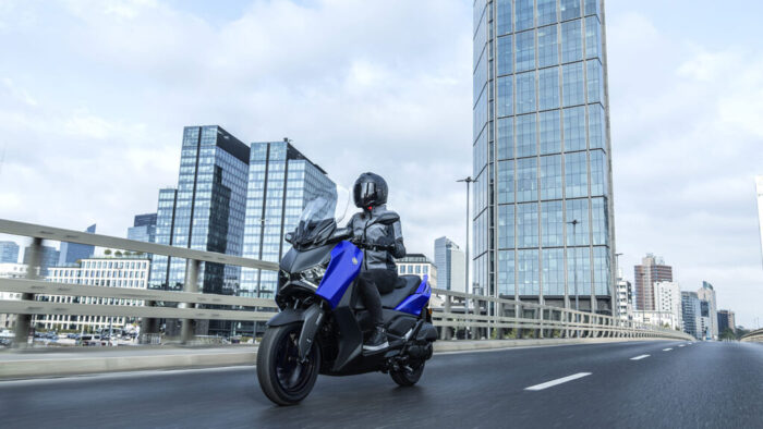 XMAX 125 v modri barvi med sodobnimi stolpnicami – samozavesten mestni skuter za vsakodnevne poti.