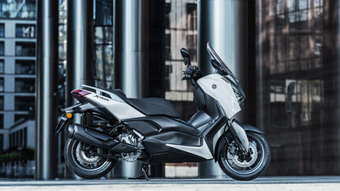 Yamaha XMAX 300 Tech MAX parkiran pred sodobno arhitekturo – prestižni maxi skuter z značajem.