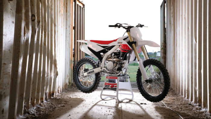 Yamaha YZ450F 70th Anniversary 2026 postavljena na stojalu v industrijskem ambientu, poudarek na posebni 70th Anniversary grafiki in dirkalni zasnovi